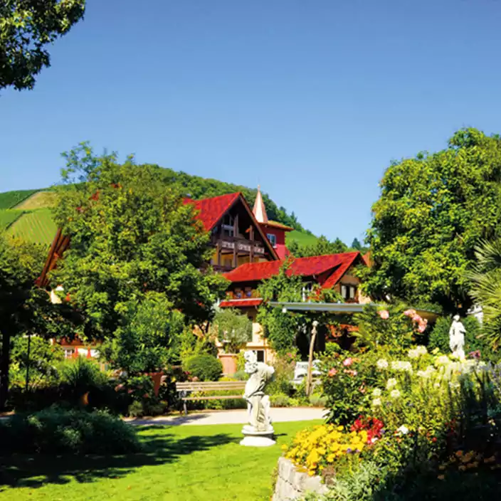 Außenansicht eines Hotels mit roten Dächern, umgeben von gepflegtem Garten und Skulpturen im Schwarzwald